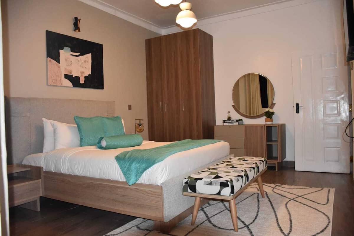 Une chambre à coucher comprenant un lit, une table de chevet, une commode, un miroir et un tableau accroché au mur.
