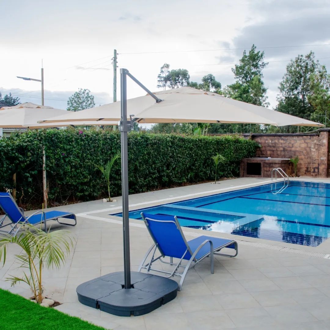 A swimming pool with lounge chairs and umbrellas, surrounded by greenery and a stone wall.