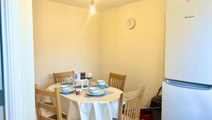 Un petit coin repas avec une table ronde, quatre chaises, une horloge au mur et un réfrigérateur blanc.