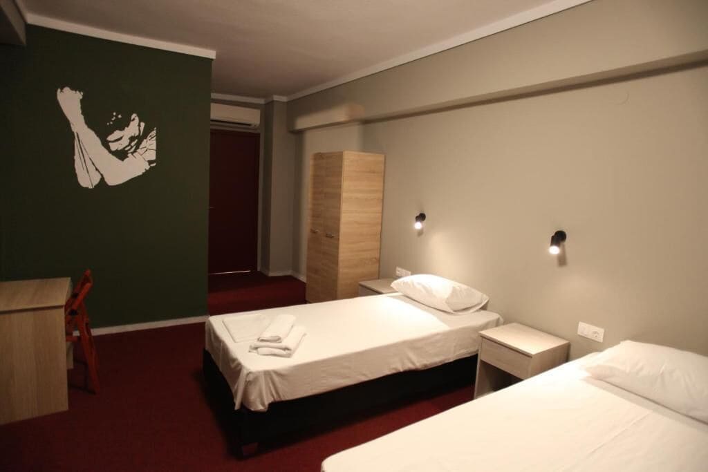 A hotel room with two beds, a desk, a chair, and a wardrobe.