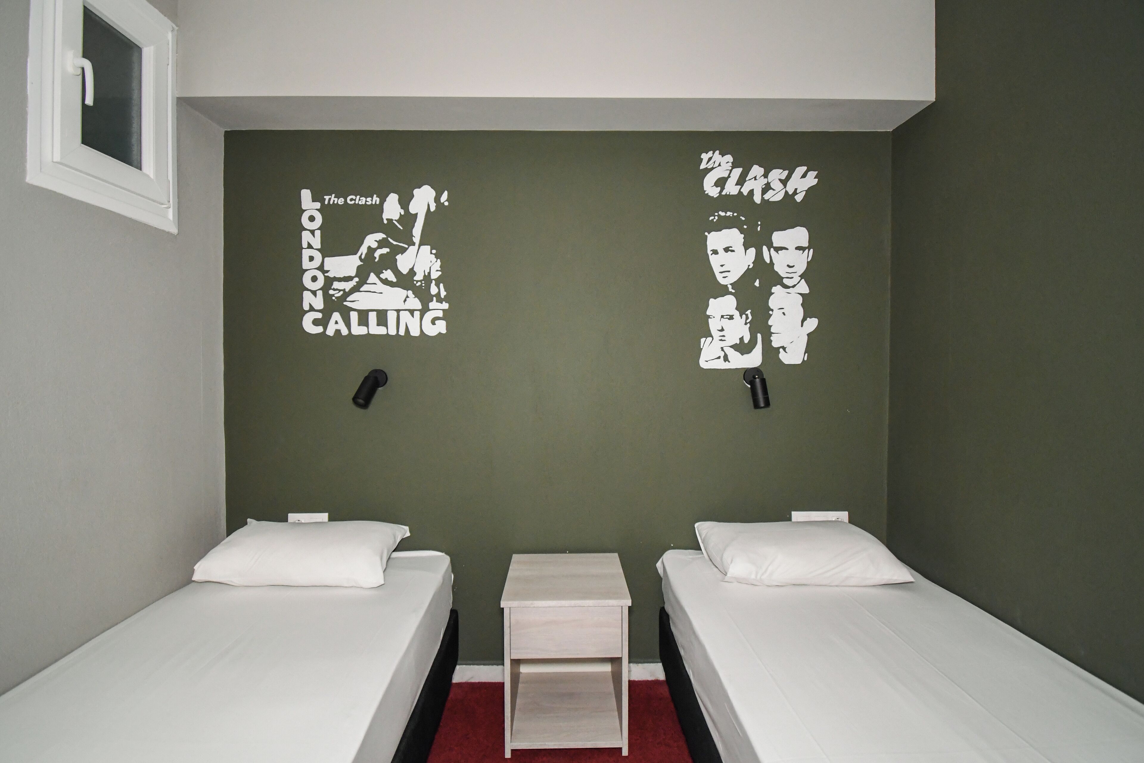 Ein Zimmer mit zwei Einzelbetten, einem kleinen Nachttisch und einer Wand mit einem grafischen Design.