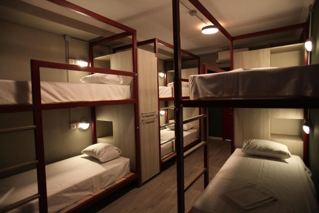 Habitación tipo dormitorio con literas, cada una con almohada y una mesita de noche pequeña.