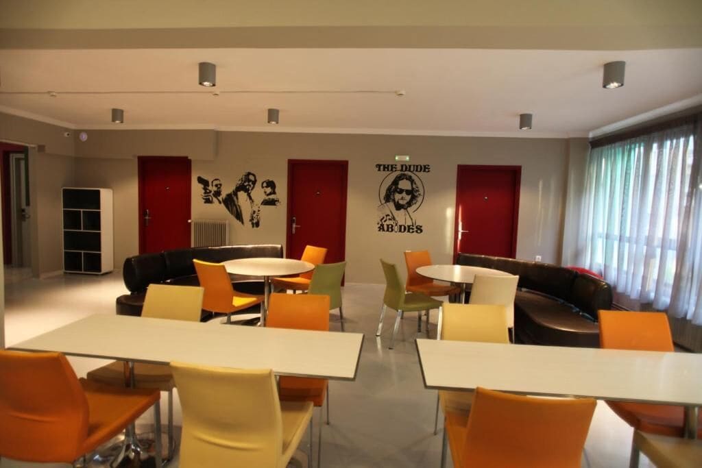 A modern lounge area with tables and chairs, red doors, and a wall with a band poster.