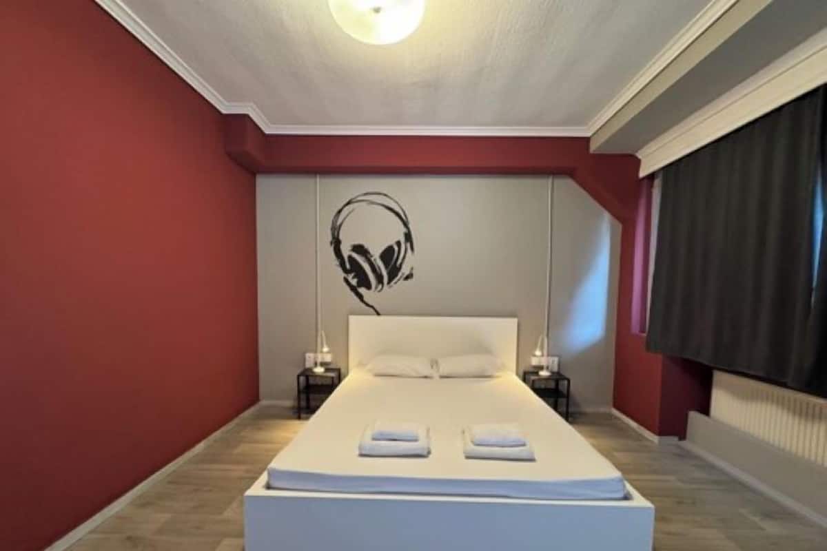 Une chambre moderne avec un grand lit, une tête de lit dotée d’écouteurs et un mur d’accent rouge.