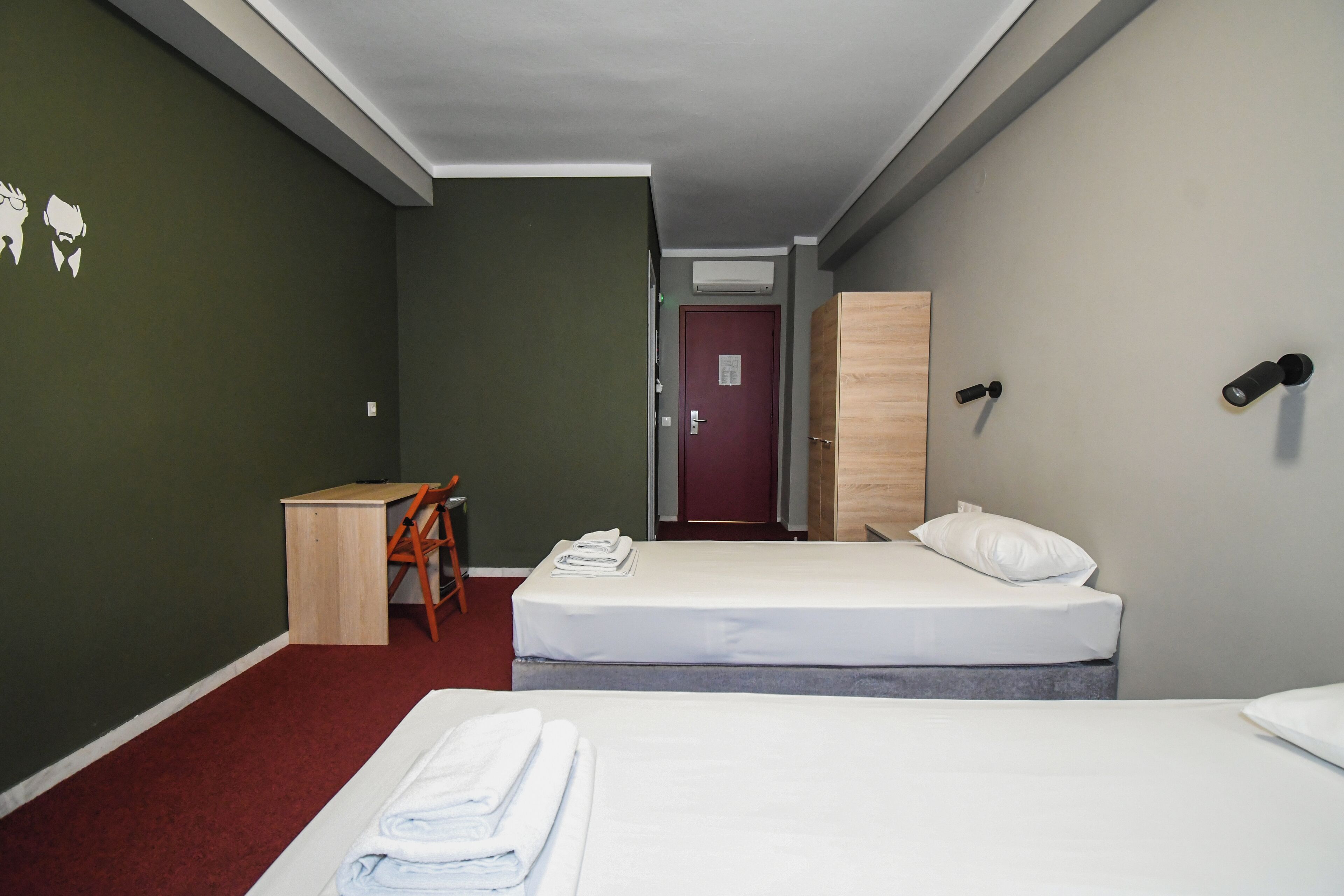 Et hotelværelse med to senge, et skrivebord og en stol.