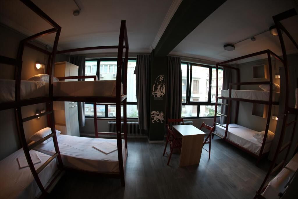 A dormitory-style room with bunk beds, a wooden desk, and a chair.