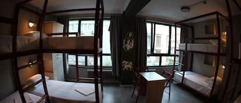 A dormitory-style room with bunk beds, a wooden desk, and a chair.