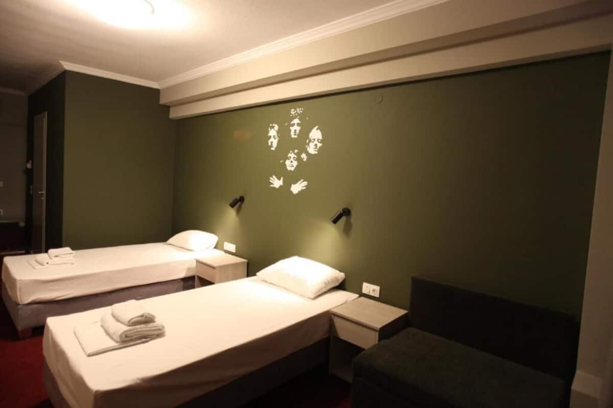 Une chambre d’hôtel avec deux lits simples, un petit coin salon et un mur vert orné d’un motif blanc.