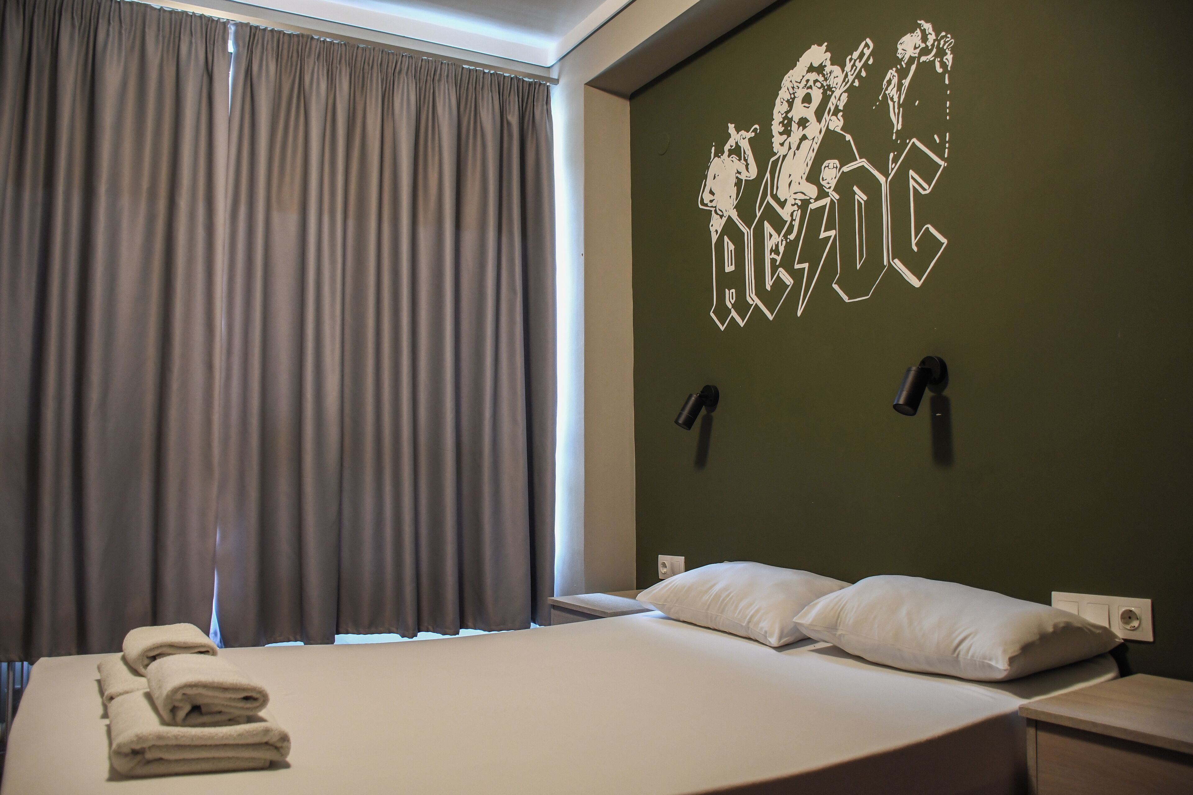 A hotel room with a bed, curtains, a wall-mounted lamp, and a wall decoration.