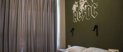 A hotel room with a bed, curtains, a wall-mounted lamp, and a wall decoration.