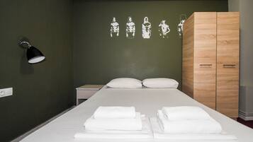 Una cama bien hecha con ropa de cama y toallas blancas, un armario de madera, una lámpara de pared y una pared con un diseño sencillo.