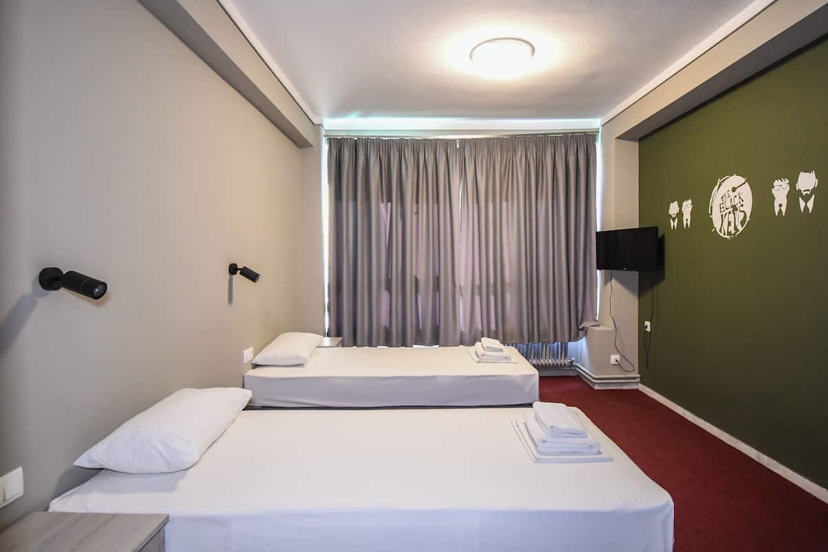 Une chambre d’hôtel avec deux lits, un téléviseur à écran plat, un radiateur fixé au mur et un mur vert orné d’un logo.