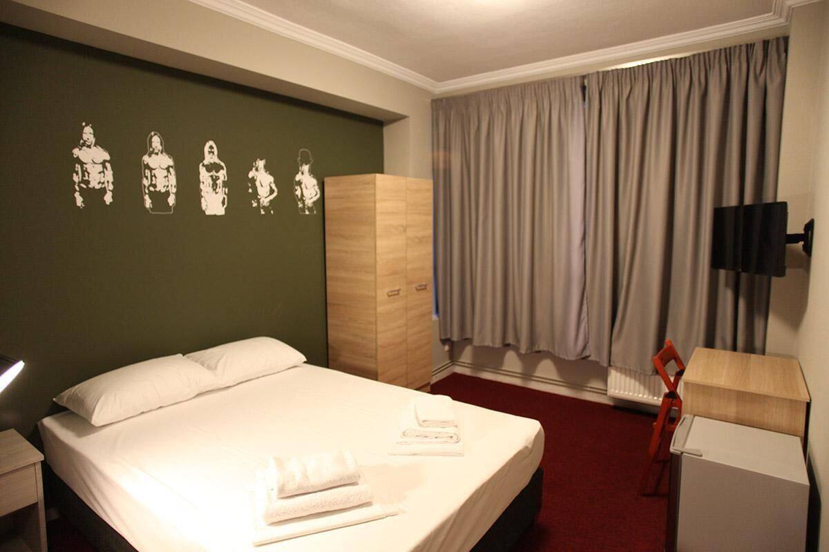 Une chambre d’hôtel comprenant un lit, une armoire, un bureau avec une lampe et un mur décoré d’œuvres d’art.