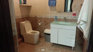 A bathroom with a toilet, a trash bin, a sink with a glass countertop, and a mirror above the sink. - Museum Hostel (Tbilisi)