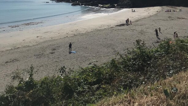 Een strand met een rotsachtige klif, mensen aan het wandelen, en een heldere lucht.