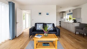 Een moderne woonkamer met een zwarte leren bank, een houten salontafel en een keuken op de achtergrond.