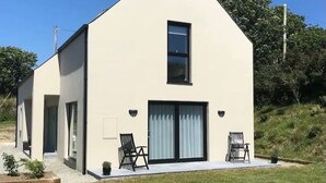Een modern gelijkvloers huis met een grote schuifdeur, twee buitenstoelen en een kleine tuin.