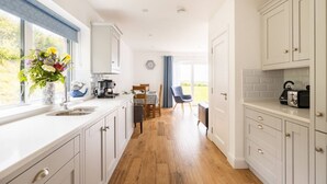 Een moderne keuken met witte kasten, een houten vloer, een eethoek met tafel en stoelen en een uitzicht op de omgeving door grote ramen.
