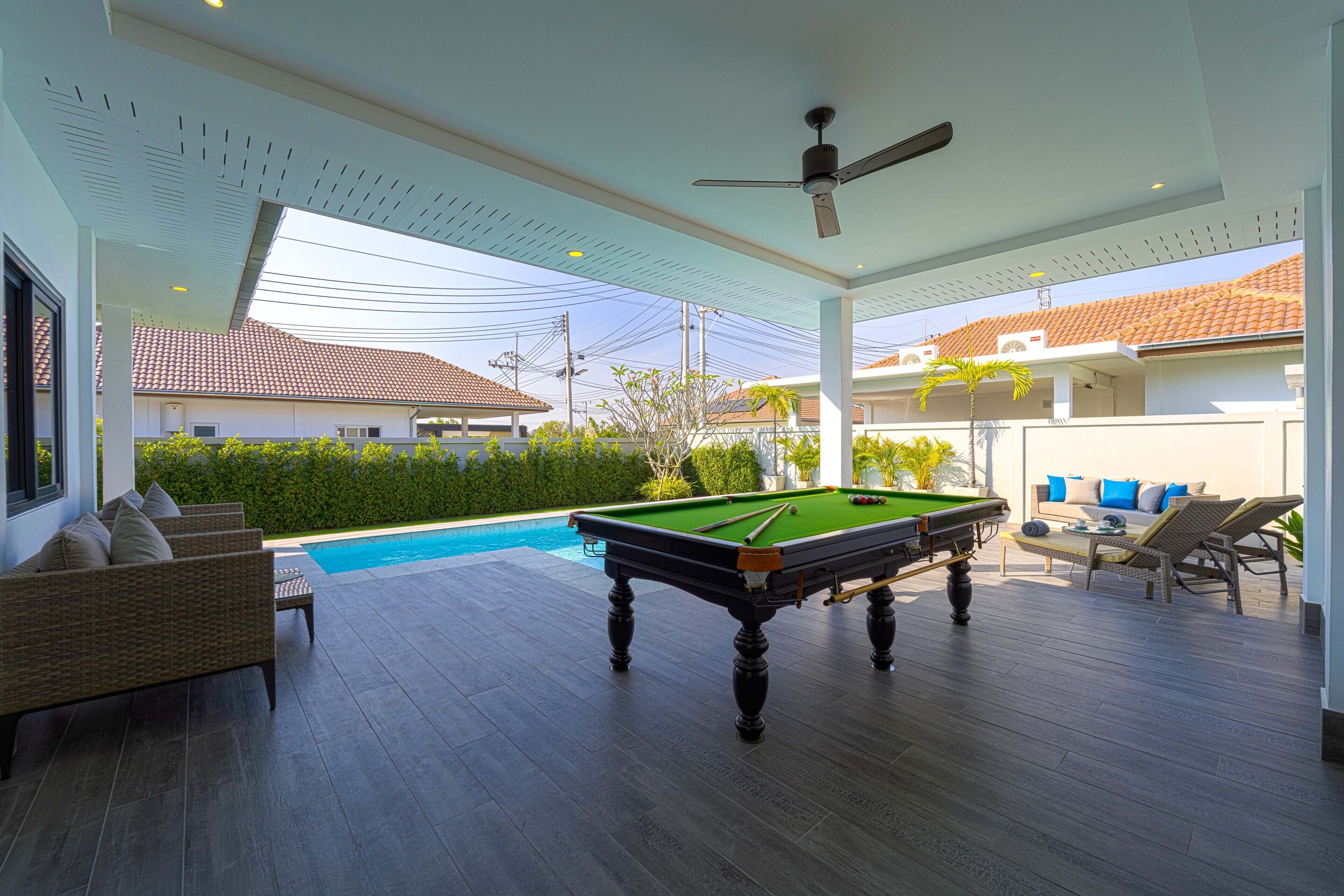 Ein Außenpoolbereich mit Billardtisch, Liegestühlen und Deckenventilator.