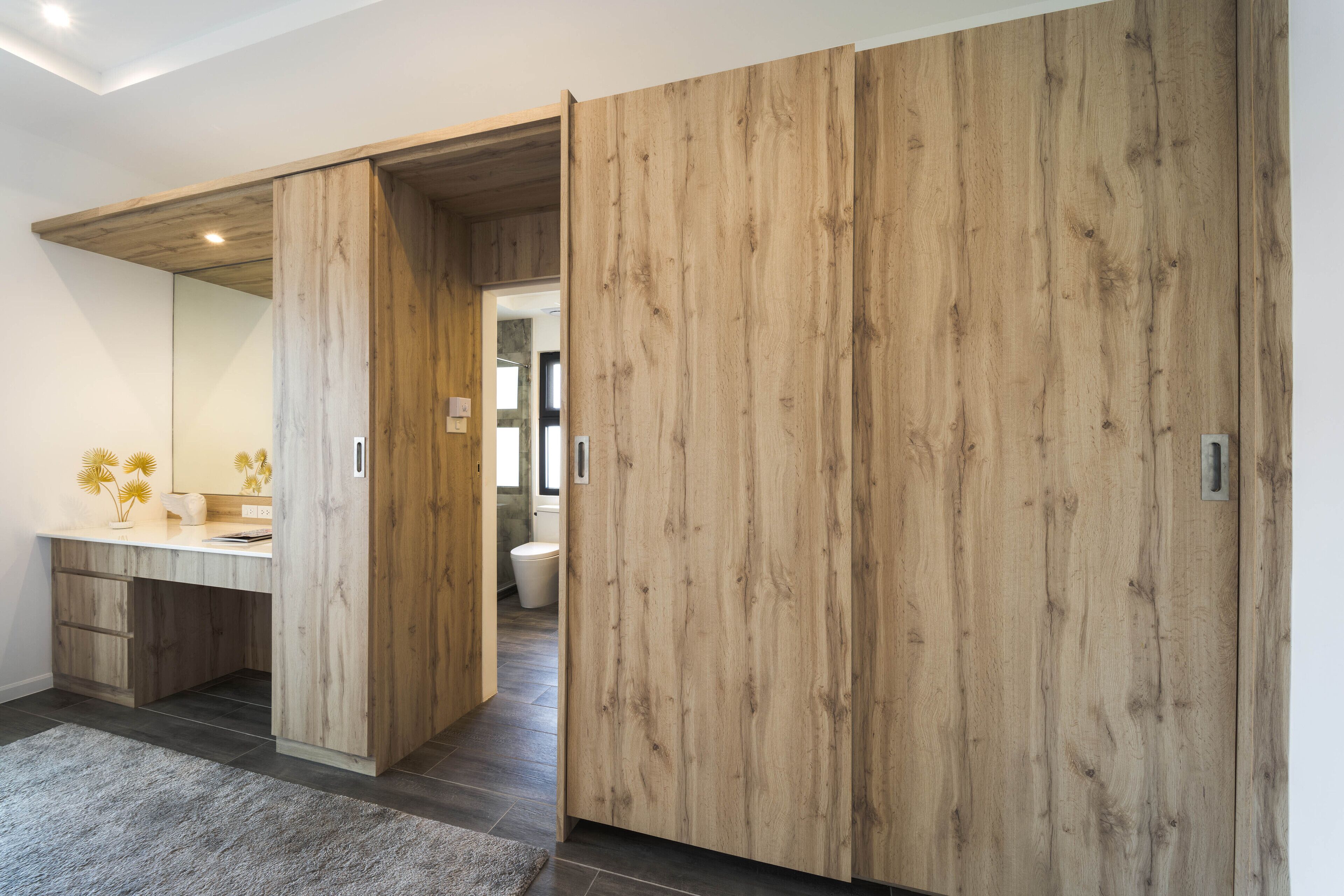 Un baño moderno con tocador de madera, un espejo grande y un inodoro a la vista a través de una puerta abierta.