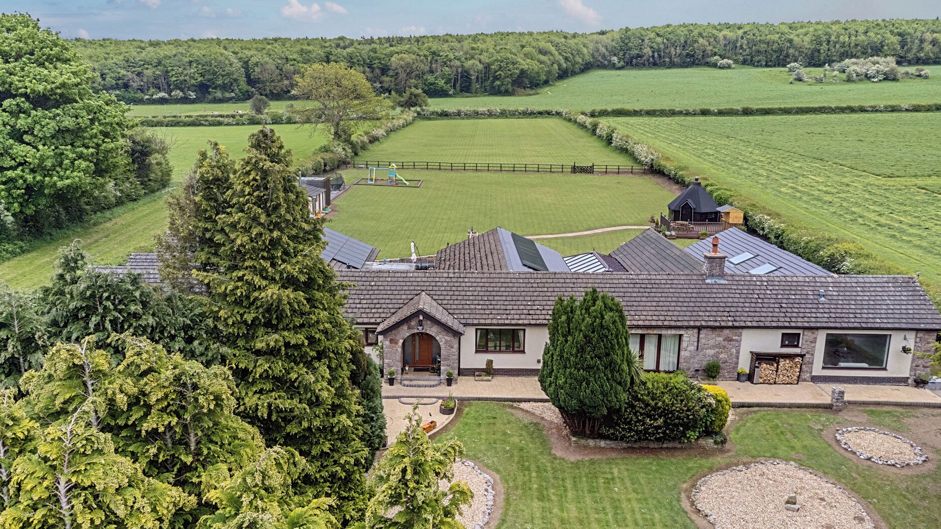 A large house with a spacious lawn, a fenced play area, and a chimney.