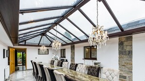 Uma sala de jantar espaçosa com uma mesa comprida e várias cadeiras, um candelabro e uma parede de pedra.