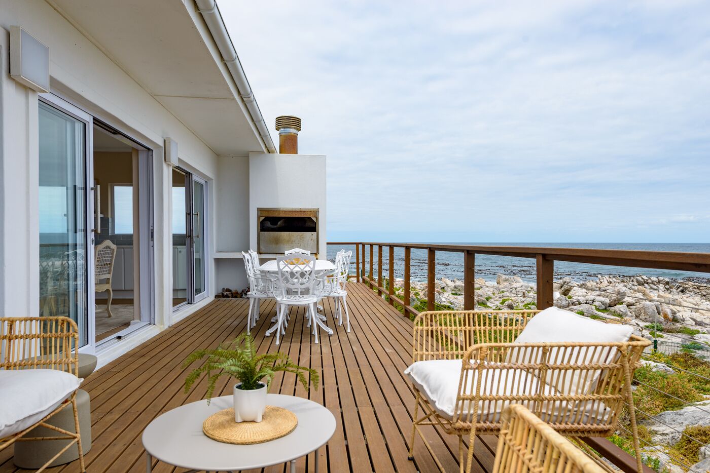 A wooden deck with outdoor furniture, a grill, and a view of the rocky shoreline.