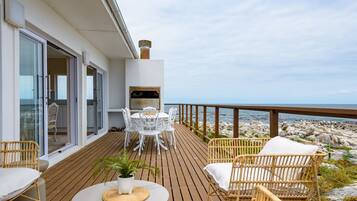 A wooden deck with outdoor furniture, a grill, and a view of the rocky shoreline.