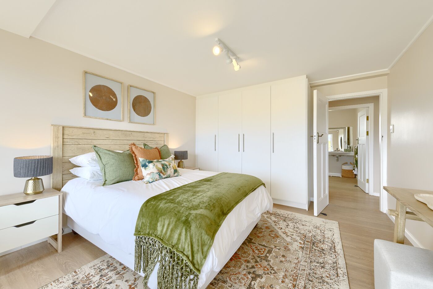 Une chambre à coucher comprenant un lit, des tables de chevet, une armoire et un couloir menant à la salle de bain.