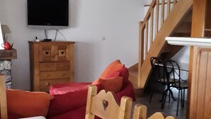 A room with a bed, wooden chairs, a TV, a wooden cabinet, and a staircase.