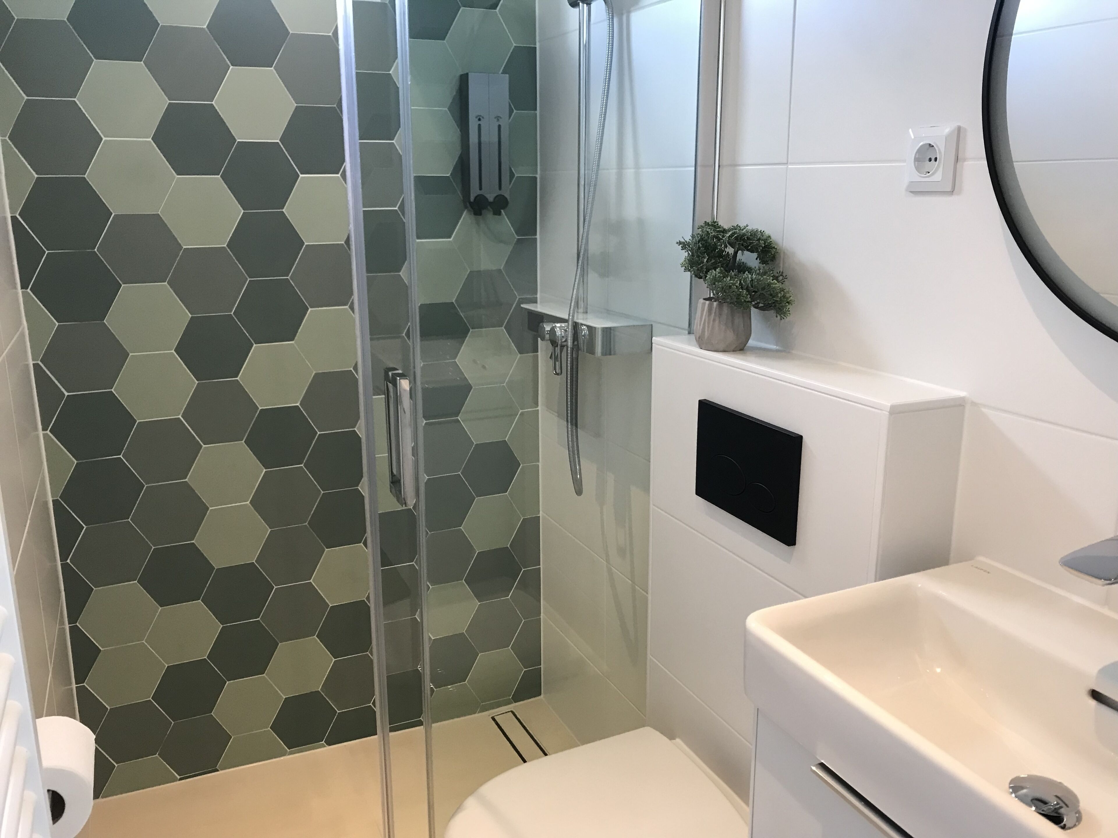 A modern bathroom with a glass shower enclosure, a white sink, and a hexagonal tile backsplash.