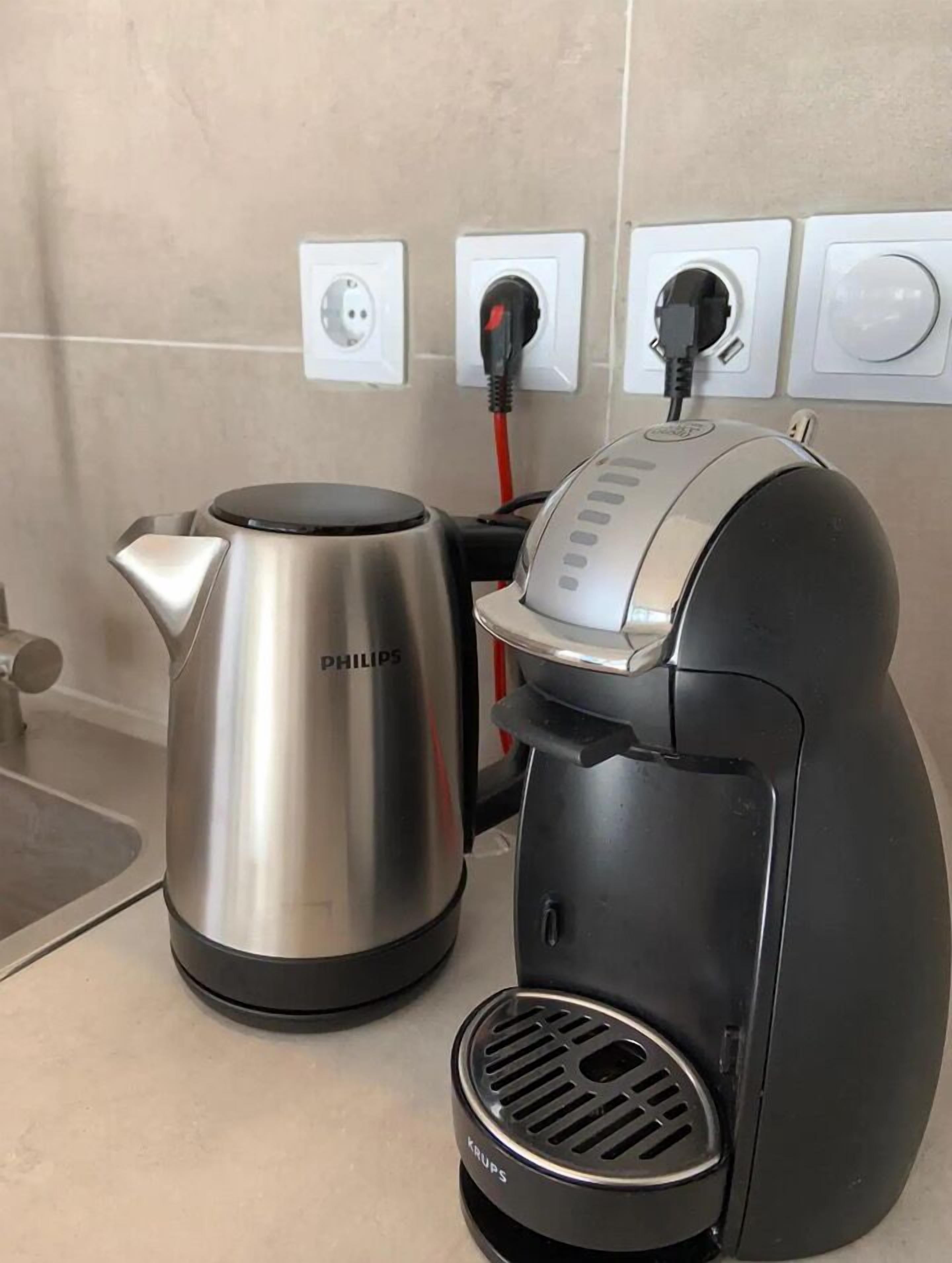 A coffee maker and a kettle on a kitchen counter with a power outlet in the background.