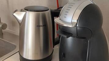 A coffee maker and a kettle on a kitchen counter with a power outlet in the background.