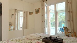 A bedroom with a bed, a chair, a mirror, and a door leading to a balcony.