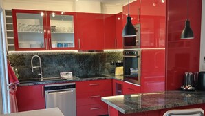 A modern kitchen with red cabinets, a granite countertop, and stainless steel appliances.