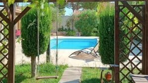 A wooden pergola with a view of a swimming pool and a wooden deck leading to a table with a vase.