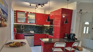 A modern kitchen with red cabinetry, a stainless steel dishwasher, and a granite countertop.