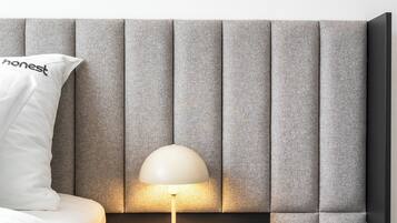 Un dormitorio moderno con un cabecero tapizado en gris, una mesita de noche con una lámpara y una almohada blanca con la palabra 'honest' escrita.
