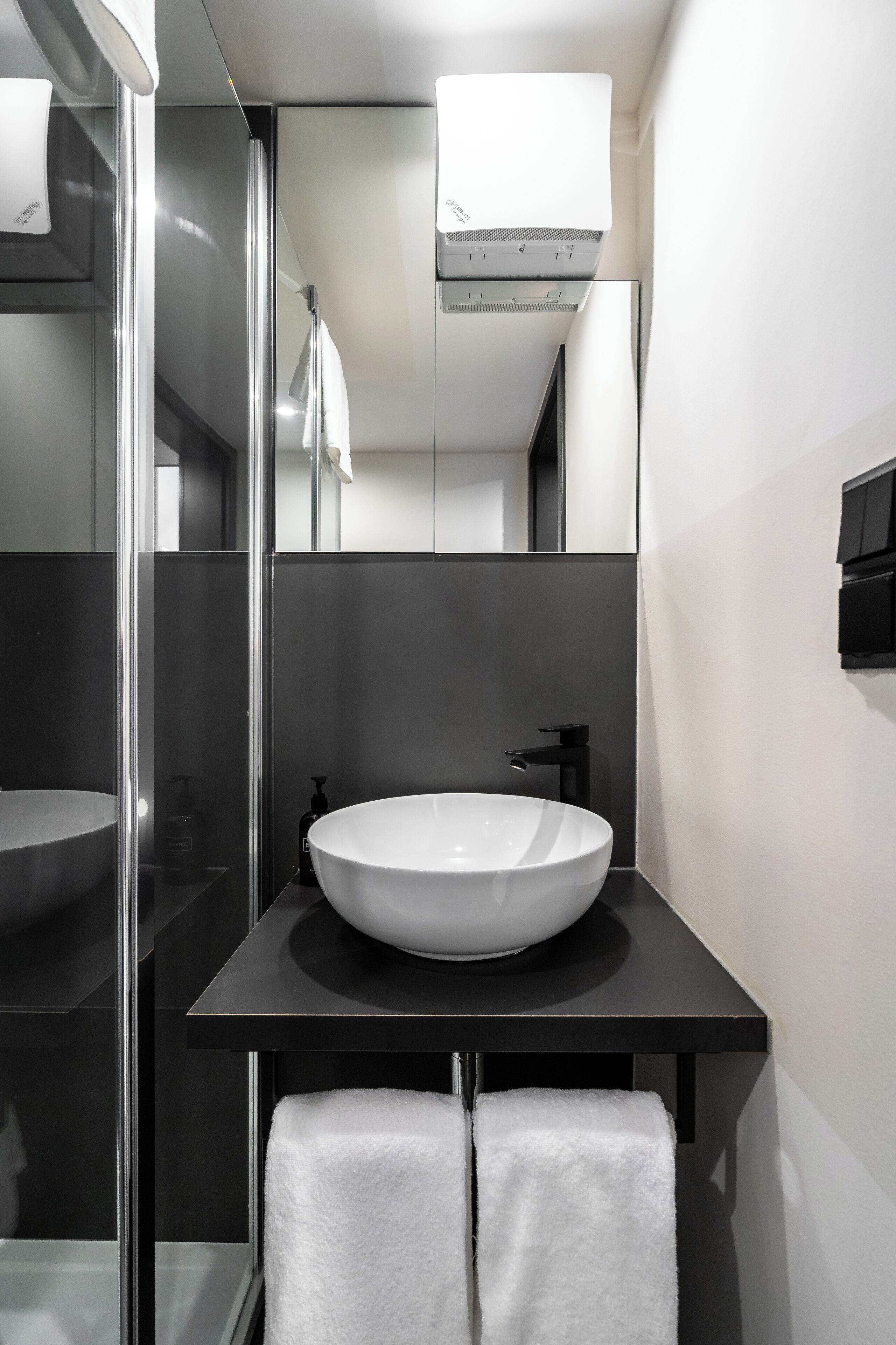 Een moderne badkamer met een groot wit wastafelmeubel, een glazen douchecabine en een zwart aanrecht.