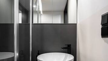 Een moderne badkamer met een groot wit wastafelmeubel, een glazen douchecabine en een zwart aanrecht.