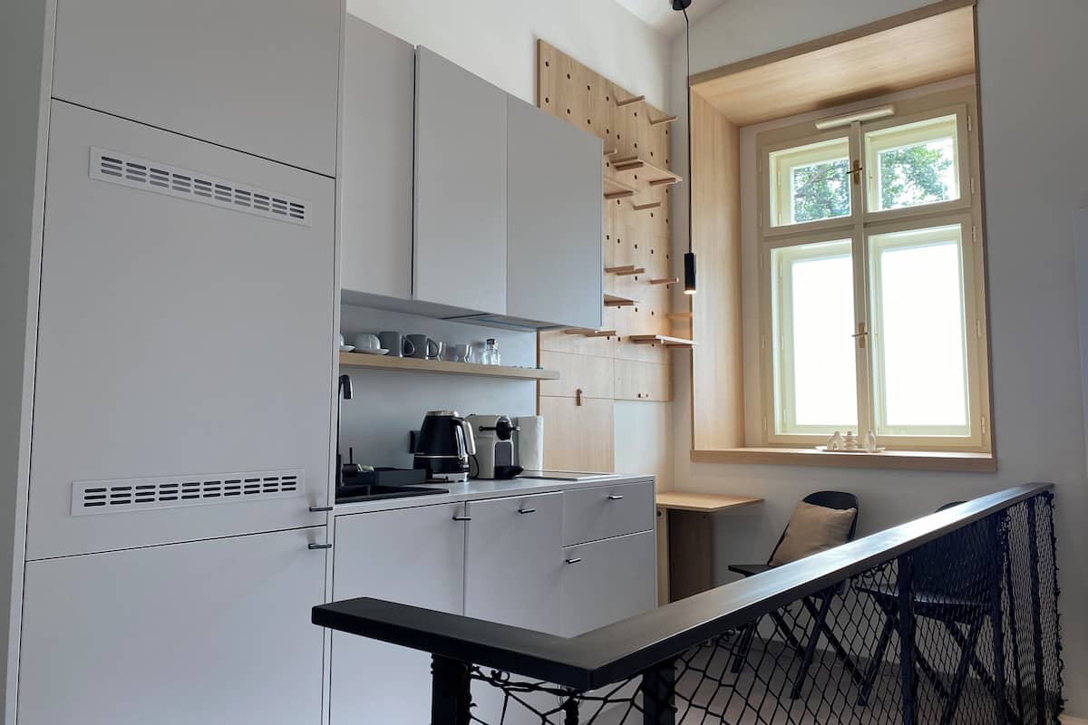A compact kitchen with white cabinets, a coffee maker, and a window with a view of trees.