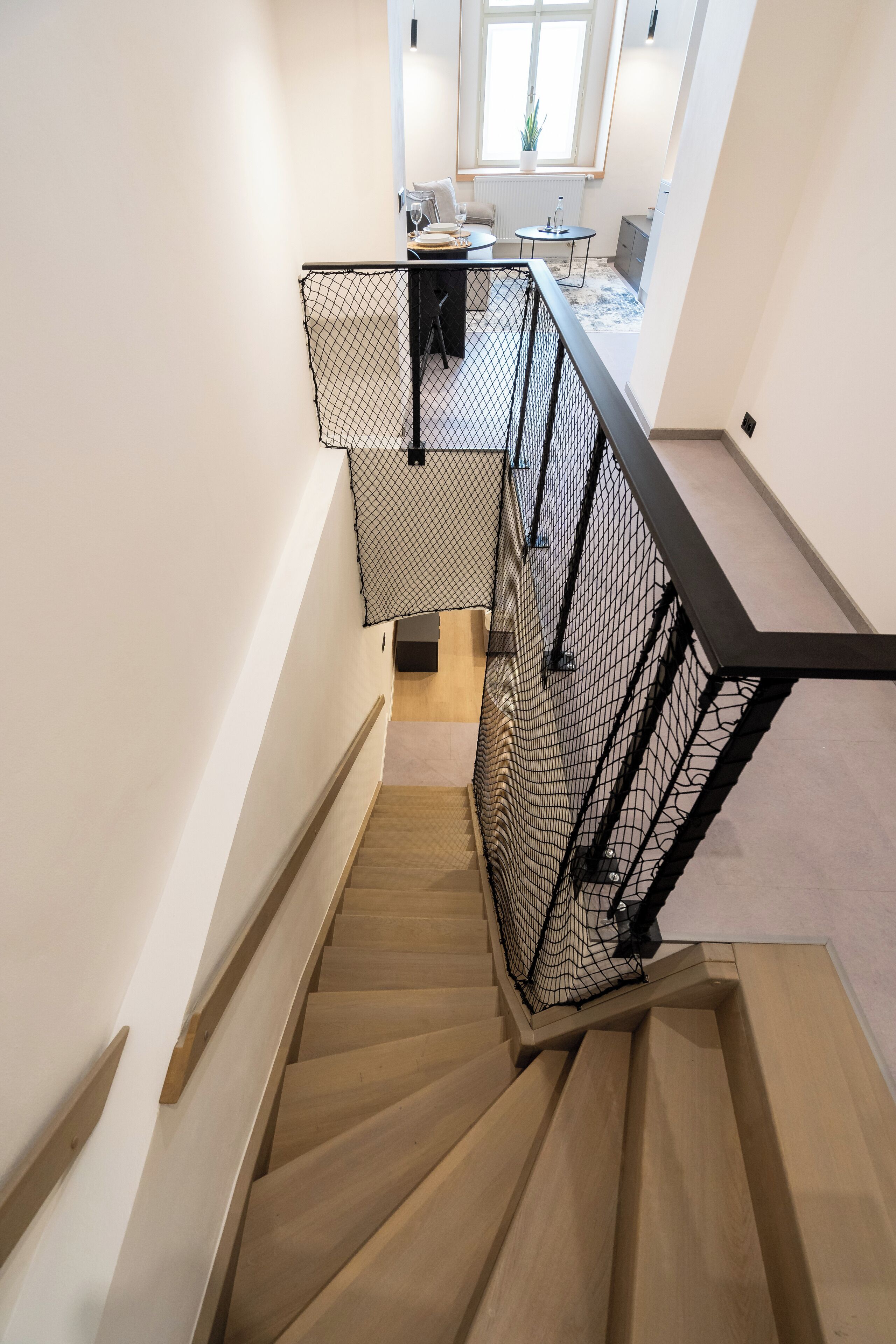 A wooden staircase with black metal railings leading to a balcony with a view of a kitchen and dining area.