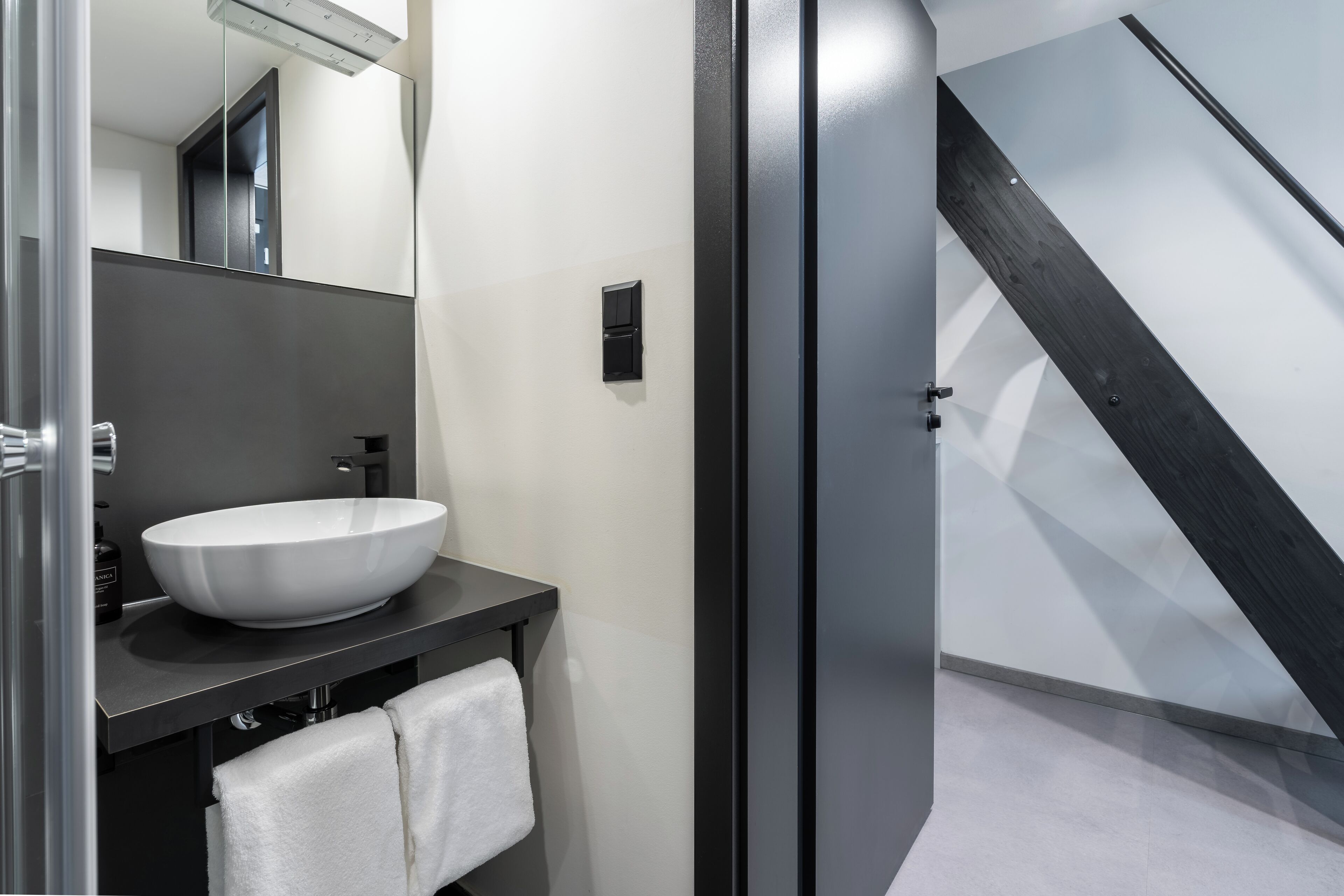 Un baño moderno con un lavamanos grande de color blanco, encimera oscura y un espejo.