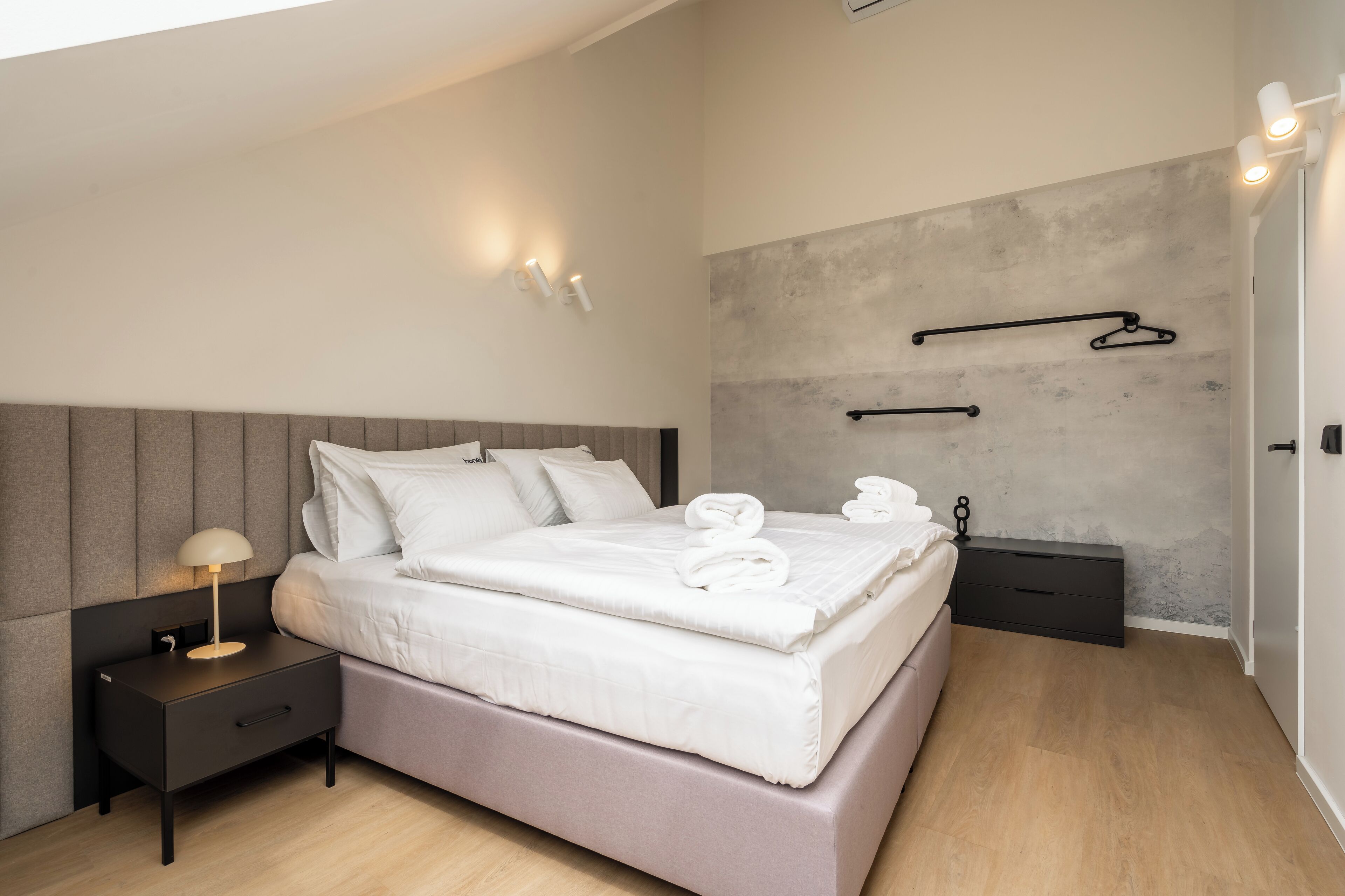 A modern bedroom with a bed, bedside table, and wall-mounted towel rack.