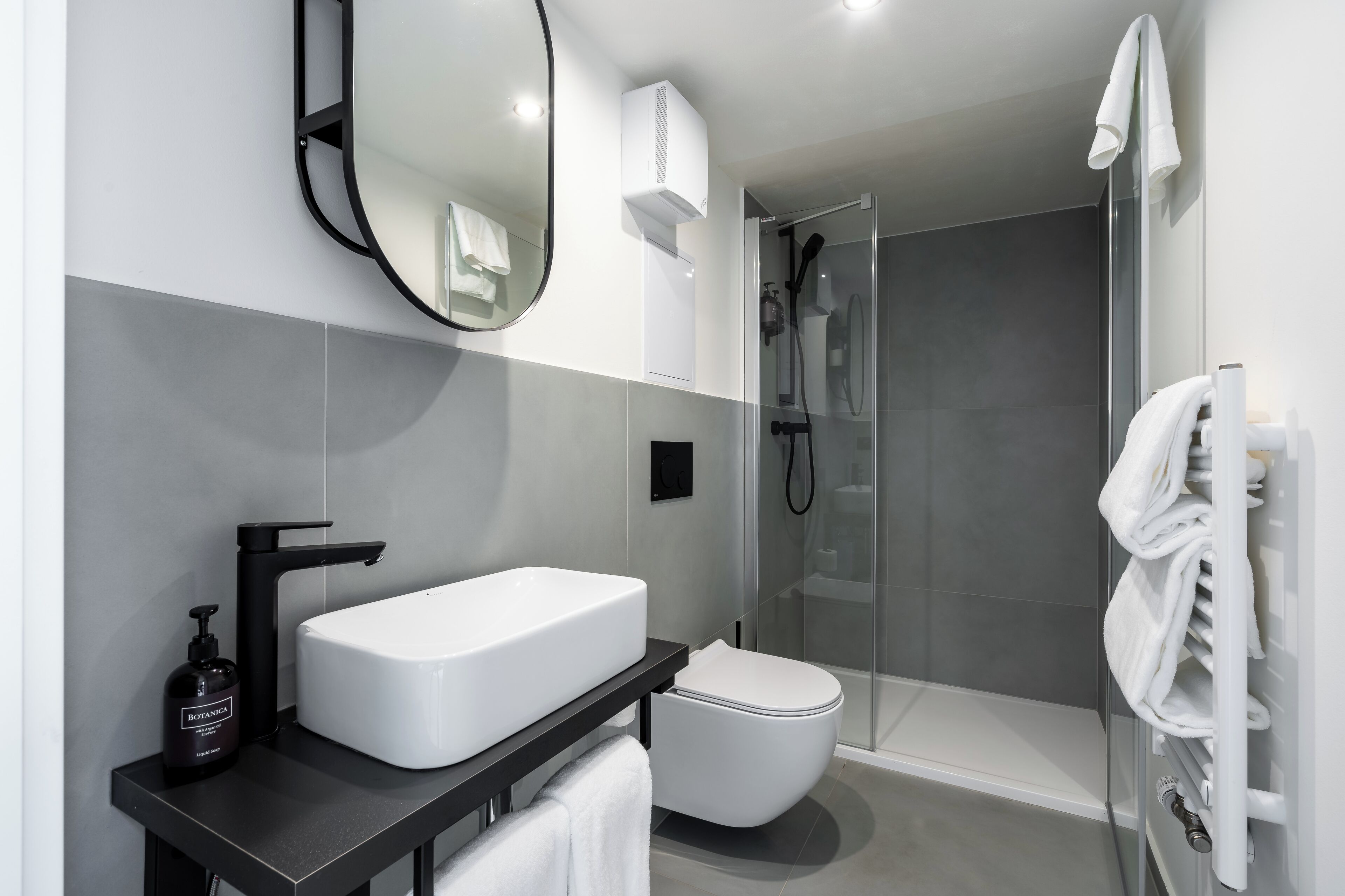 Une salle de bain moderne avec un lavabo blanc, un robinet noir et une douche à parois de verre.