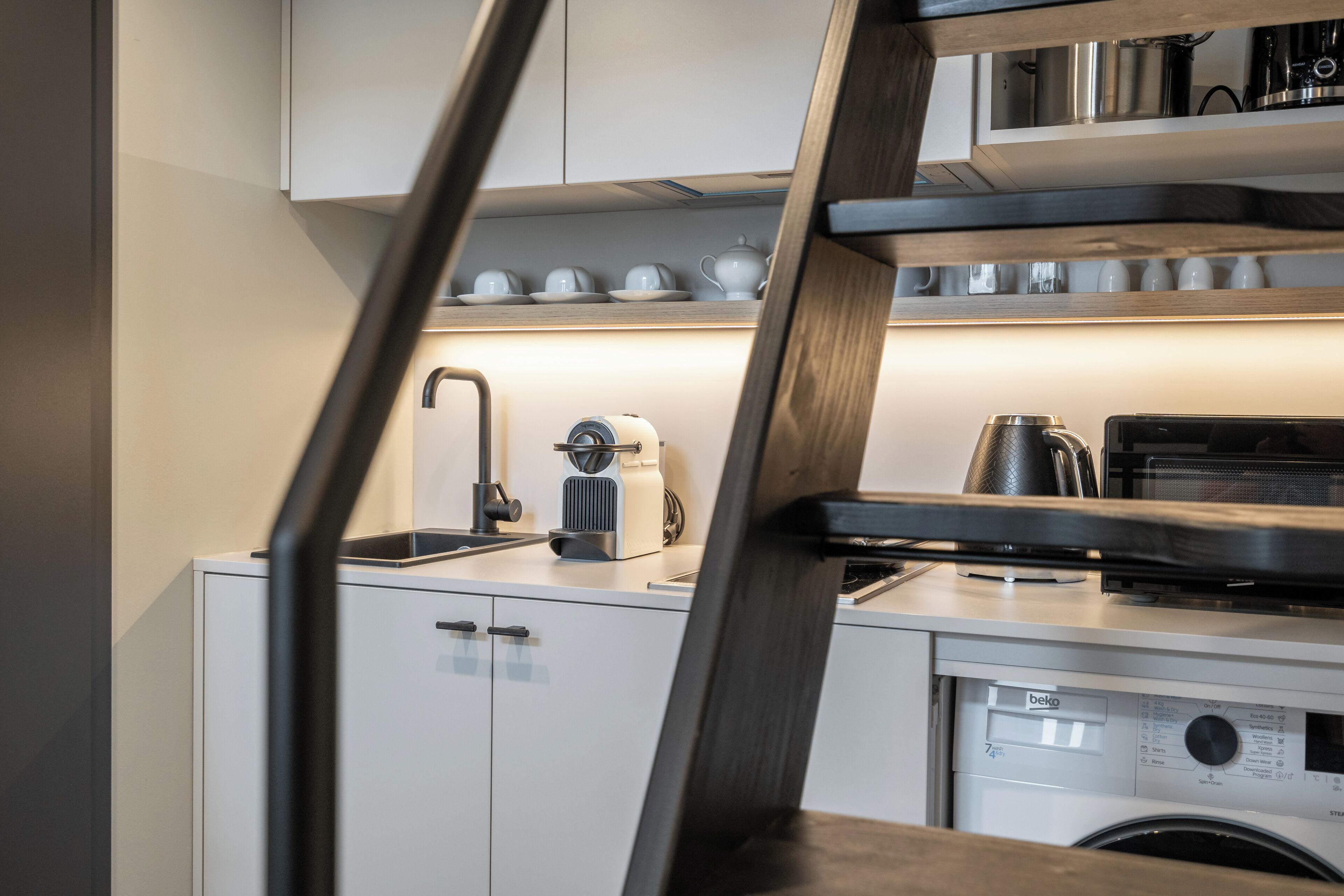 A modern kitchen with white cabinets, a coffee maker, a kettle, and a microwave.