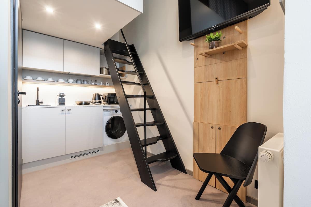 A compact kitchen with a washing machine, a black ladder, and a wooden cabinet.