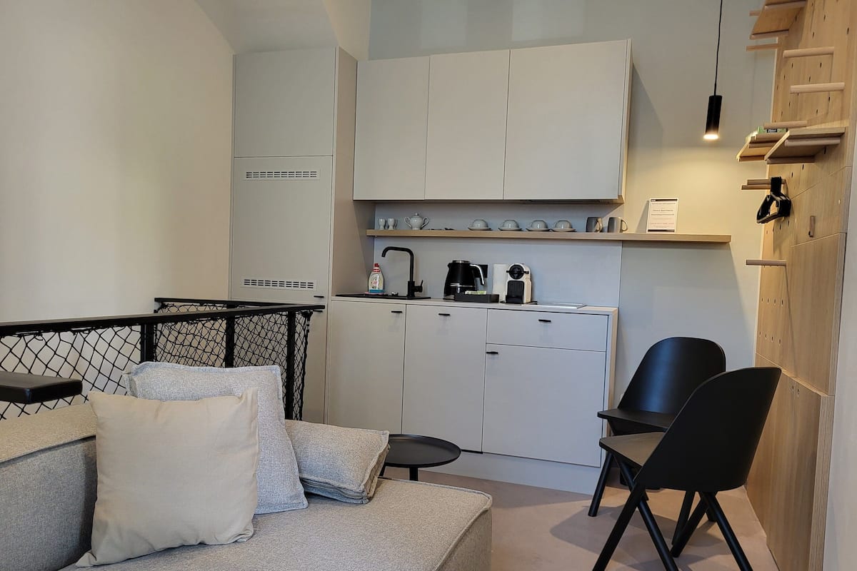 A compact living space with a kitchenette, a sofa with cushions, a dining area with a chair, and a small table.