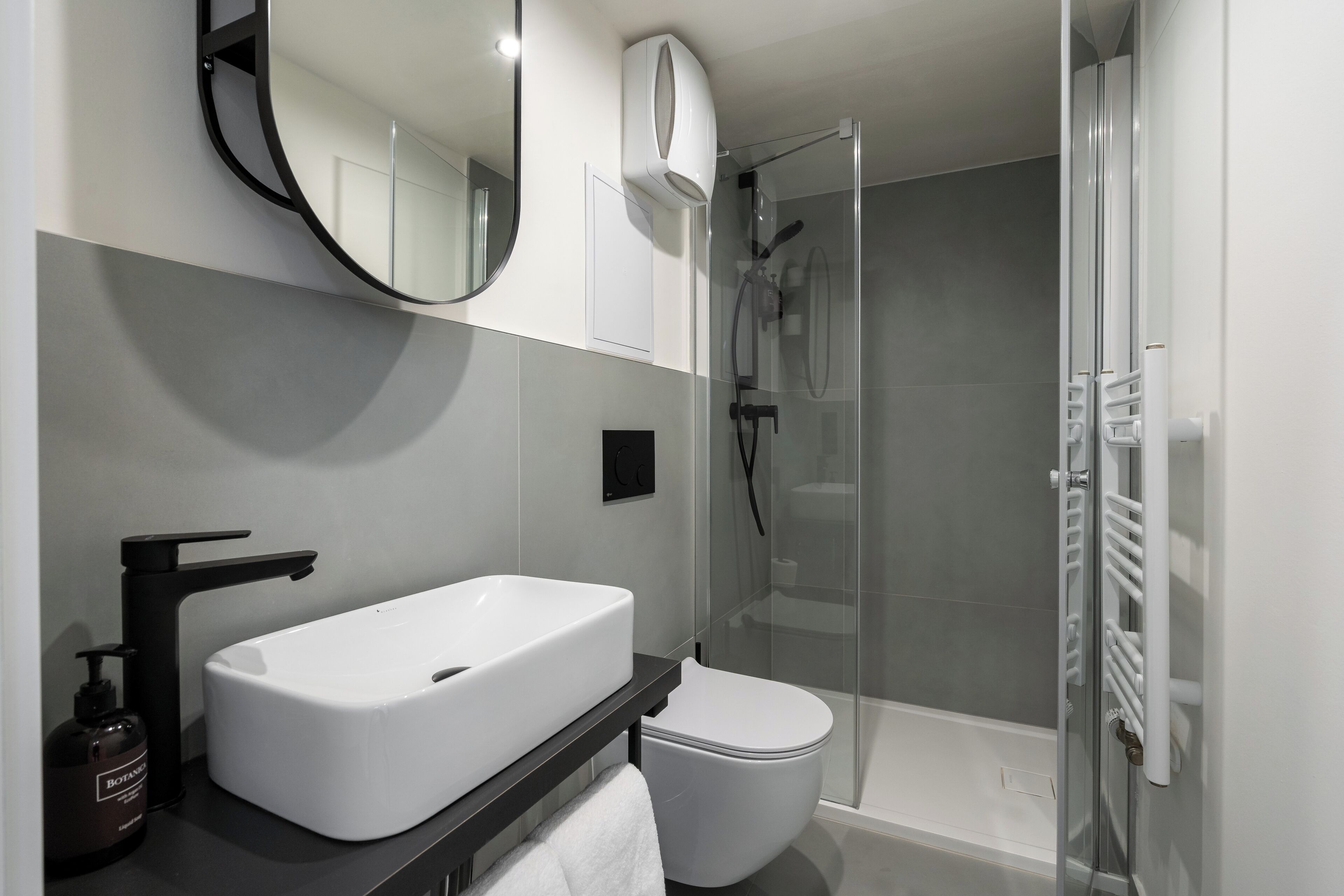 Ein modernes Badezimmer mit Waschbecken in Weiß, einem schwarzen Wasserhahn und einer Duschkabine aus Glas.