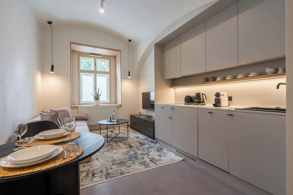 A modern kitchen with white cabinets, a dining area with a round table, and a large window providing natural light.